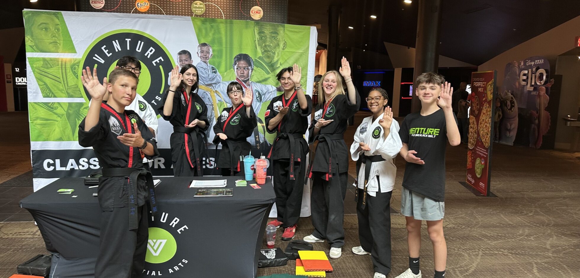 Group of martial arts students in black uniforms posing with hands raised at Venture Martial Arts event.