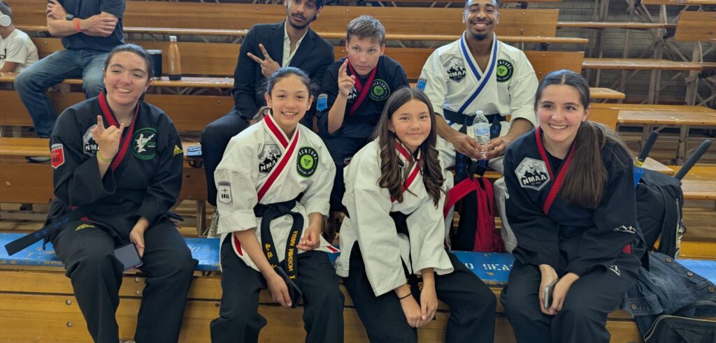 Group of martial arts practitioners in uniforms seated together, displaying various expressions and poses at an event.