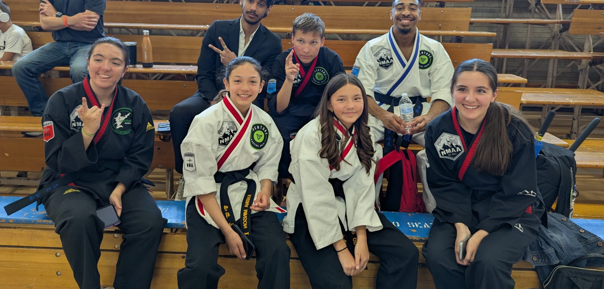 Group of martial arts practitioners in uniforms seated together, displaying various expressions and poses at an event.