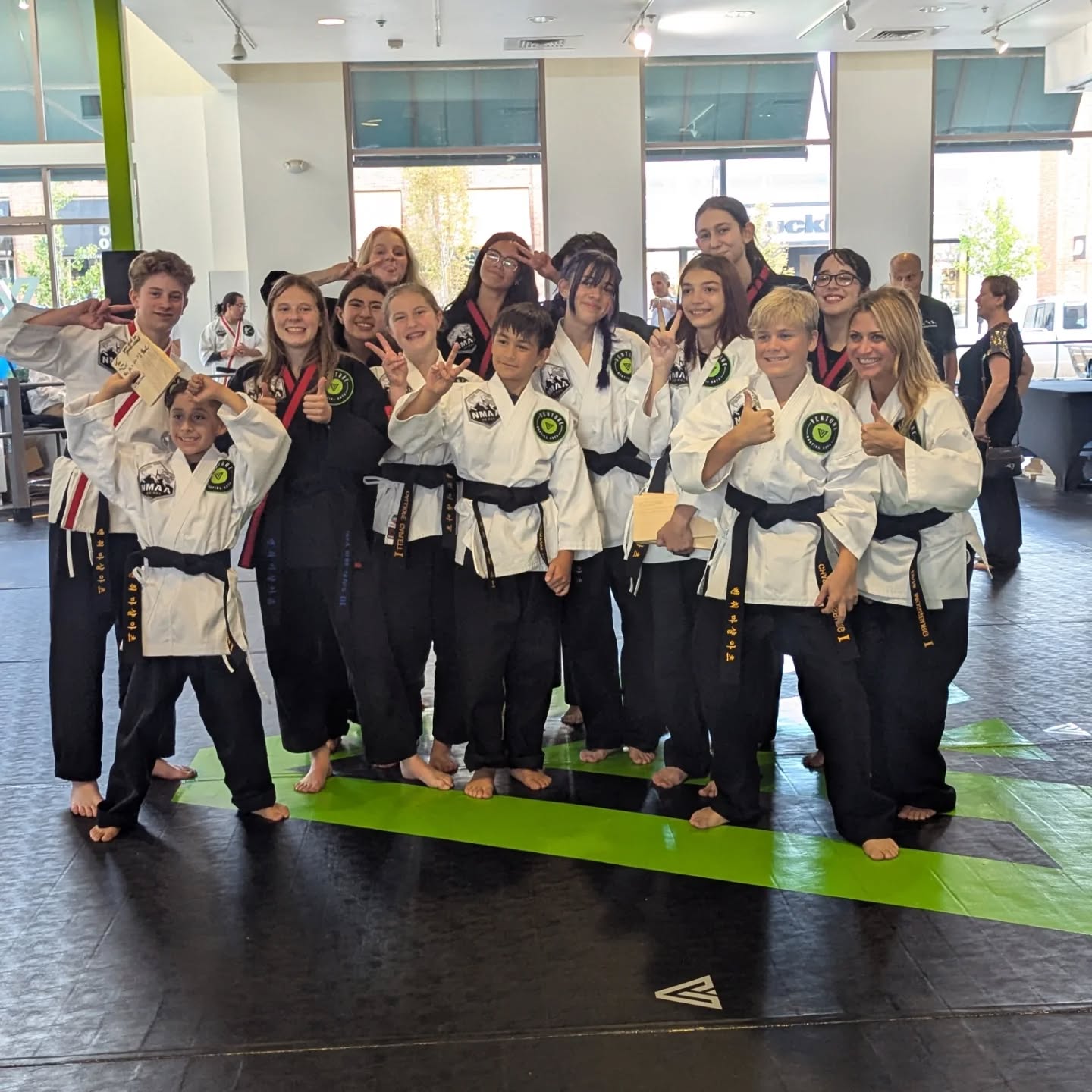 Group of martial arts students in black belts posing together, showing their certificates in a training facility.