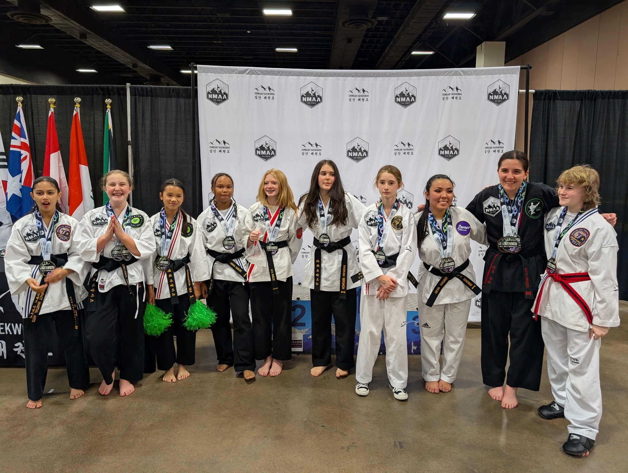 Group of young martial artists wearing uniforms and medals, posing together at a competition event.